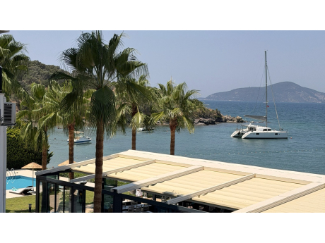 Med-Inn restaurant terrace and palm trees above Güllük Bay, with a catamaran at anchor and an island on the horizon