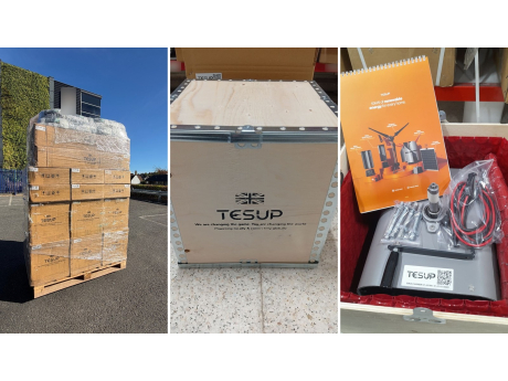 Un pallet avvolto nel film con cartoni TESUP al sole, una cassa TESUP in compensato e una cassa aperta con un corpo Atlas, fissaggi, cavi e un calendario TESUP
