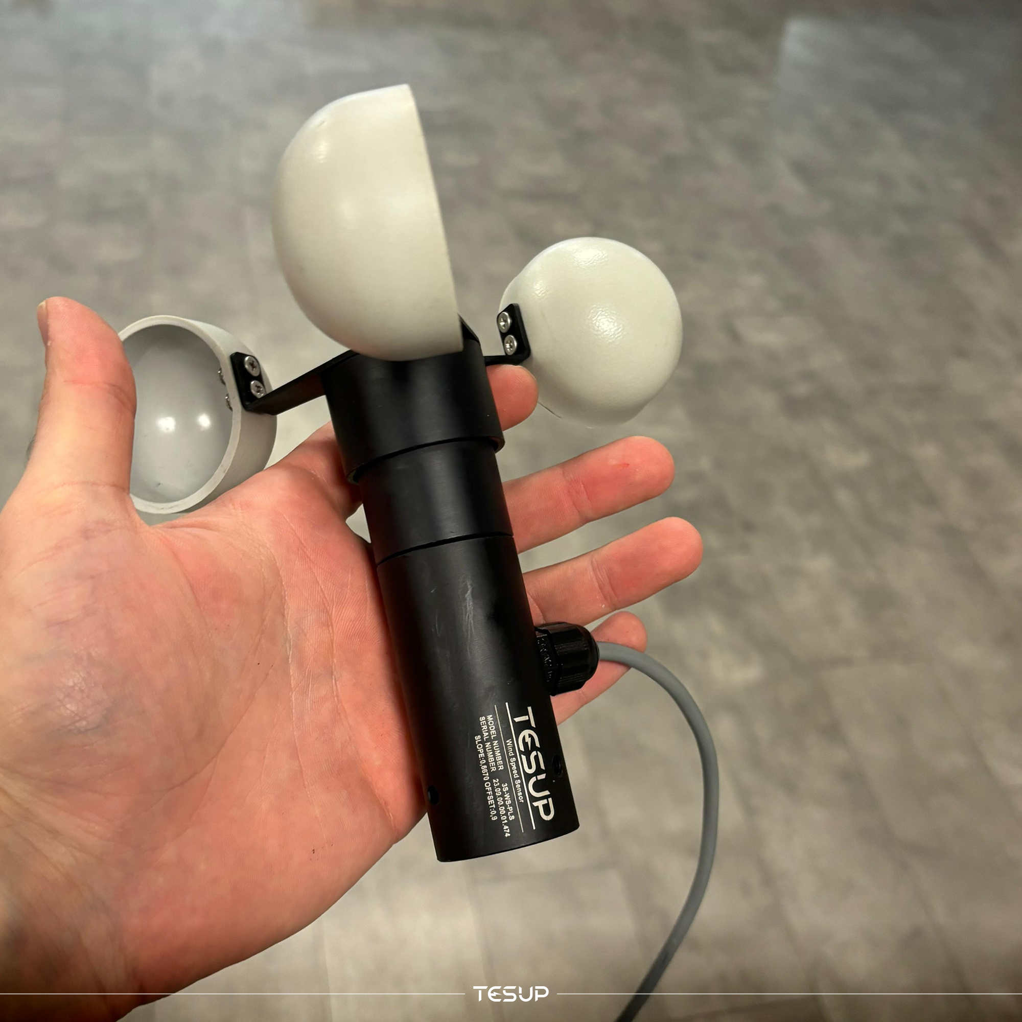 A cup anemometer held in one hand, the sensor used to measure wind speed at the site before choosing a turbine
