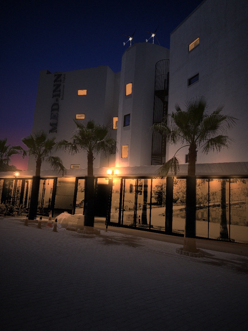 Visualisation of two white TESUP Magnum wind turbines on the roof of the Med-Inn Boutique Hotel at dusk, with the hotel lights on