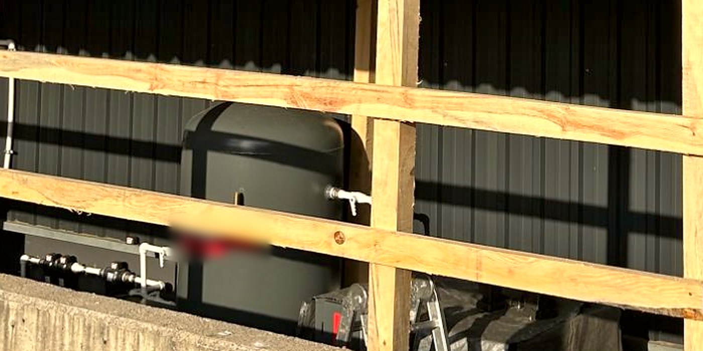 Close-up of the air receiver tank with its drain valve, gauge and air piping behind the timber rails