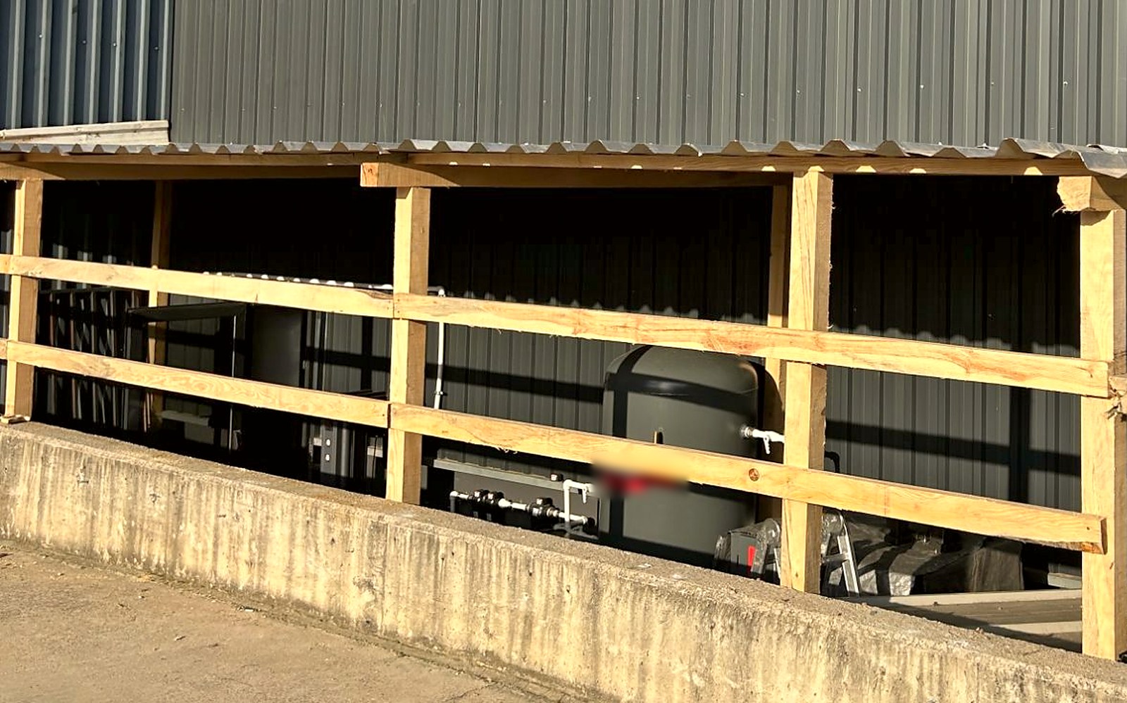 Side view of the shelter with the grey air receiver tank, piping and filters visible behind two rows of timber rails
