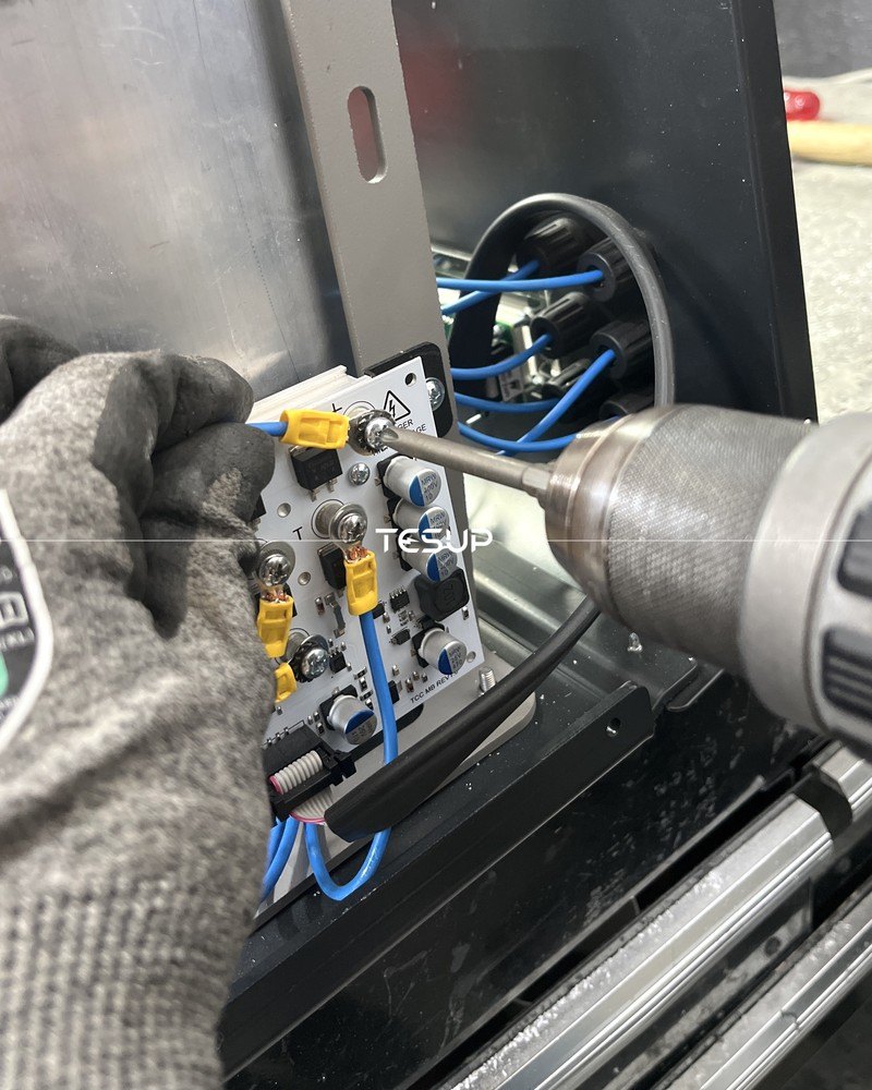 A TESUP technician wiring a charge controller circuit board with a power screwdriver