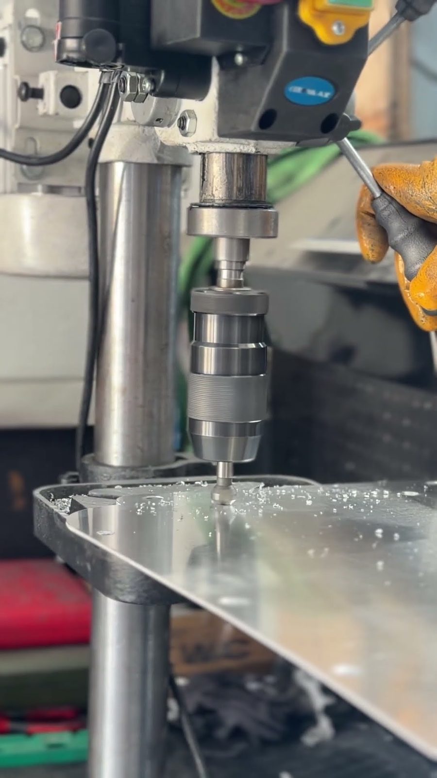Agujeros de fijación taladrándose en un panel de carcasa de aluminio en un taladro de columna, virutas repartidas por la superficie