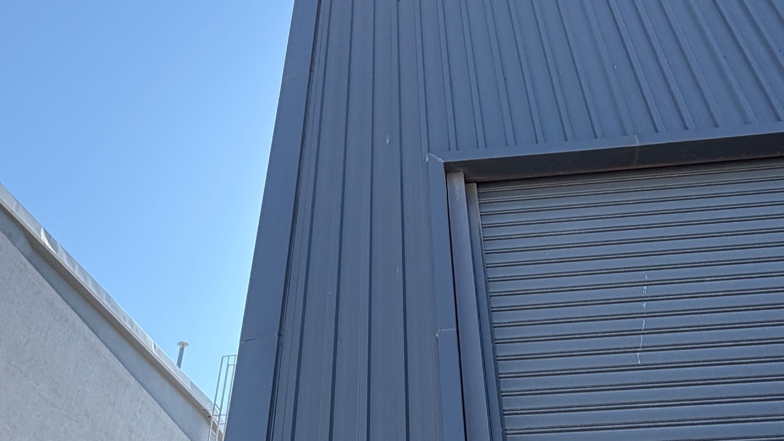 The exterior of the TESUP production building, dark grey profiled steel cladding and a roller shutter door