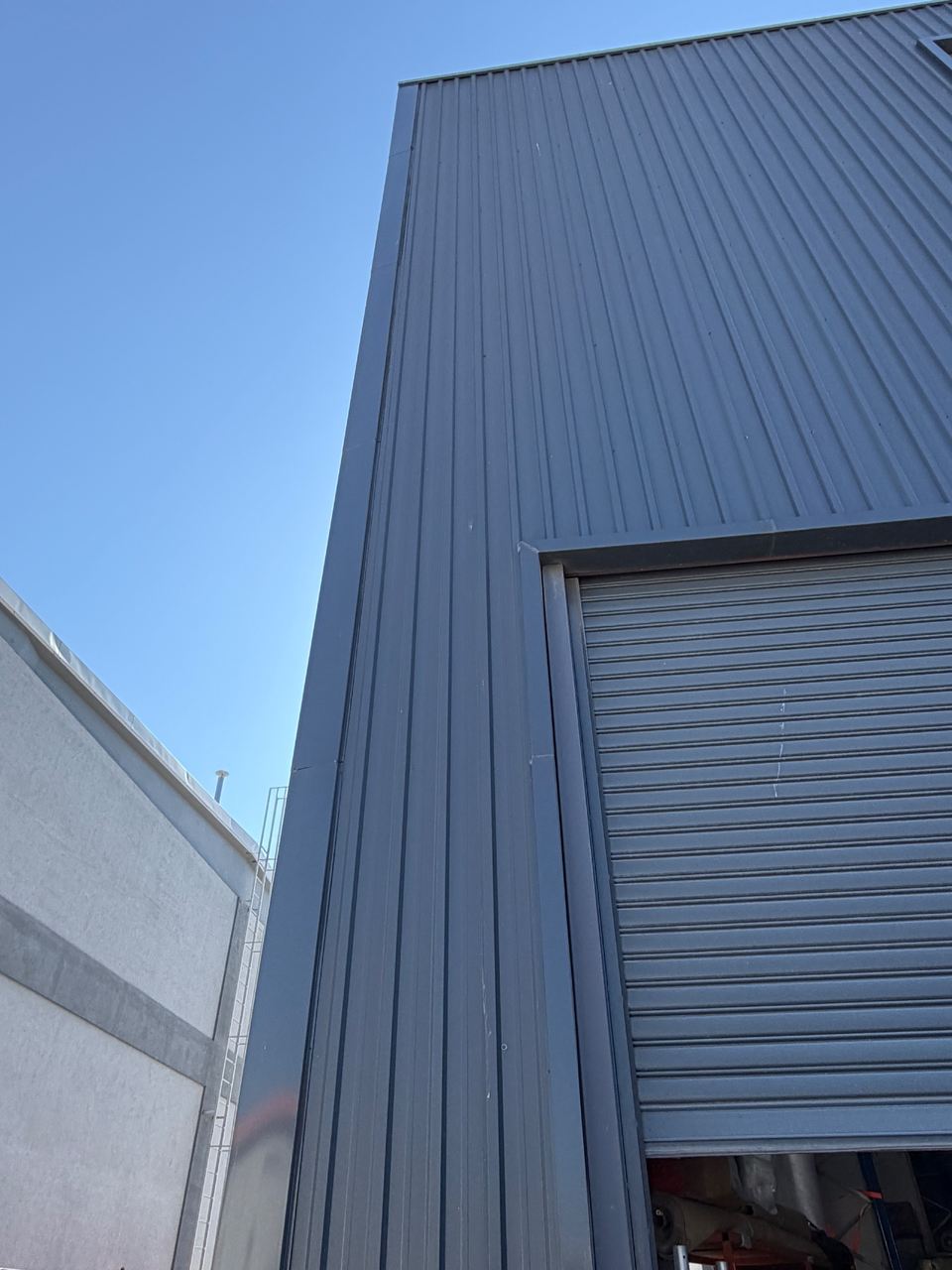 The exterior of the TESUP production building, dark grey profiled steel cladding and a roller shutter door
