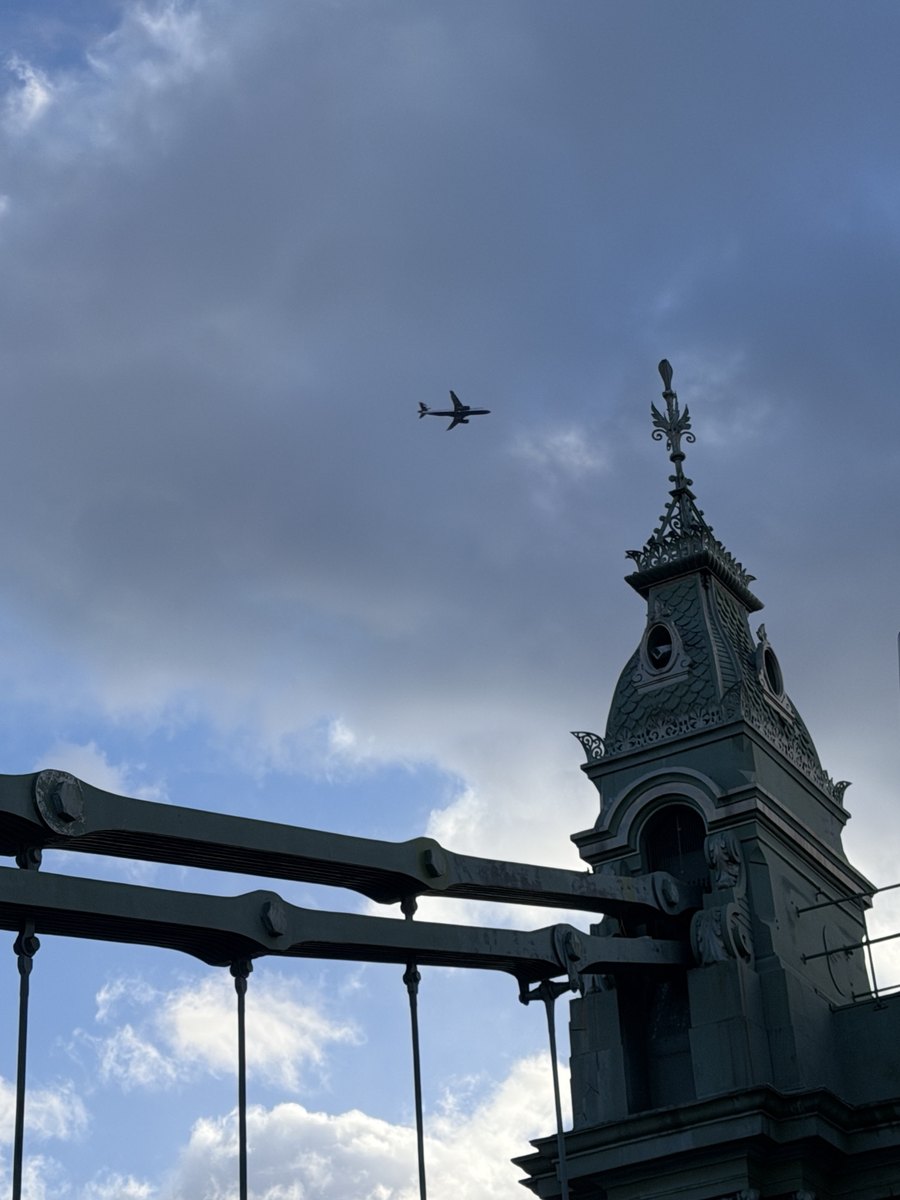One of the ornate towers of Hammersmith Bridge with a plane passing overhead