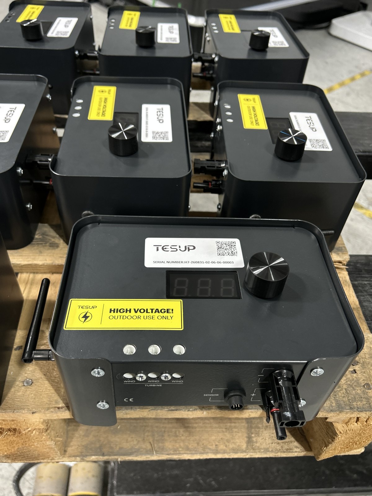 A TESUP Magnum charge controller on a pallet with its stub radio antenna screwed into the side, seen from above with several more units stacked behind it