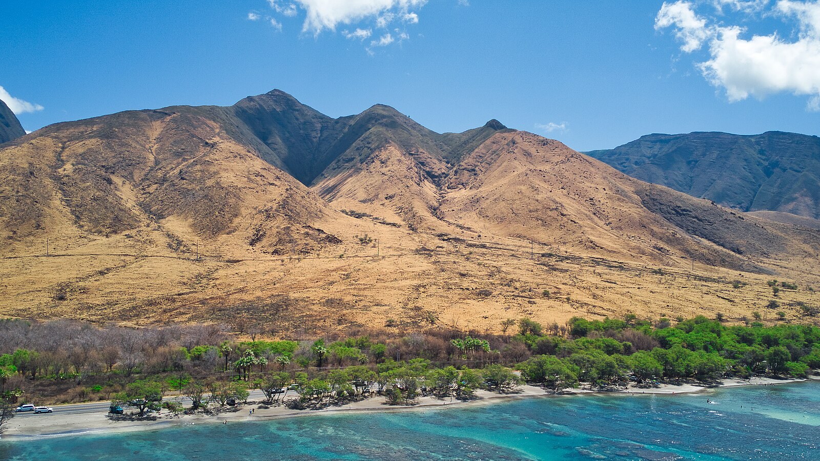 The West Maui Mountains rising above a reef-lined coast, dry brown ridges against a deep blue sea