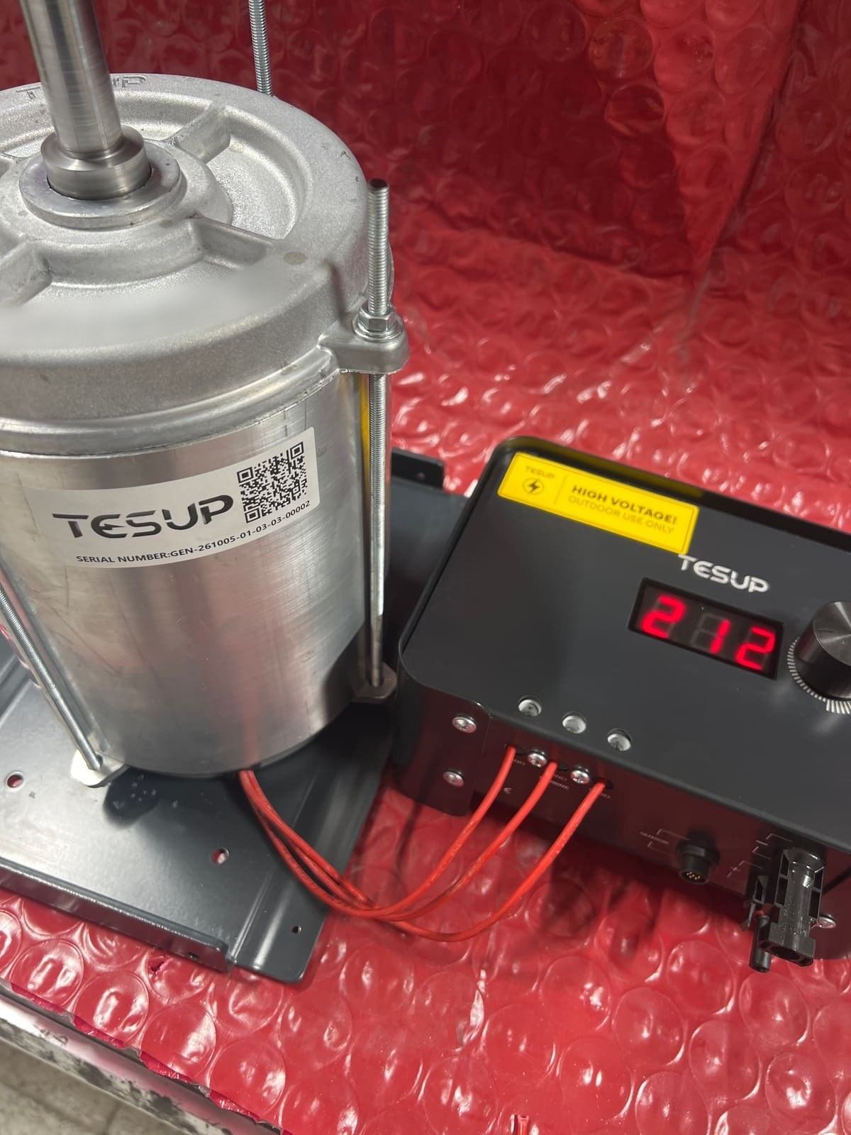 A TESUP motor/generator on the test bench, wired with three red phase wires to a TESUP charge controller showing a reading on its display
