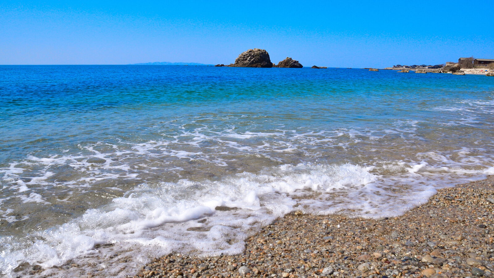 澄んだ青い海が岩場に打ち寄せる、新潟県の笹川流れの海岸