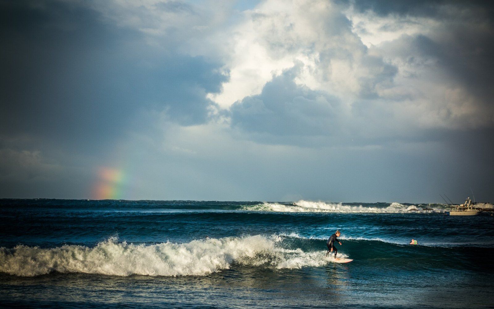 A lone surfer riding a wave under a dark storm sky with a rainbow at Terrigal Beach, New South Wales