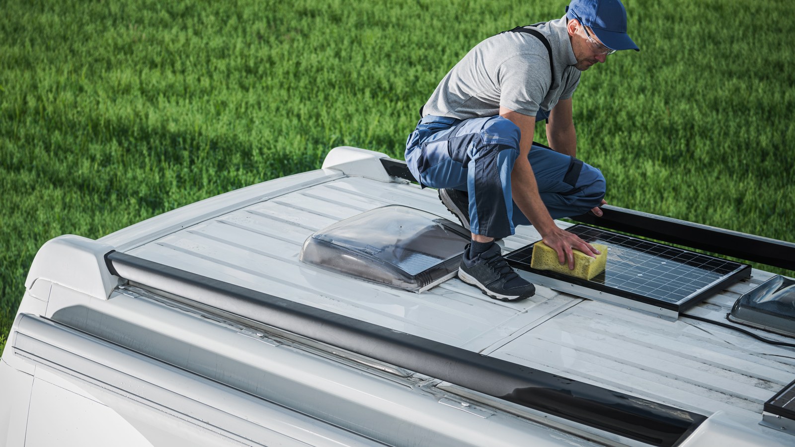 Semi-flexible solar panels bonded to the curved roof of a camper van, being cleaned by hand
