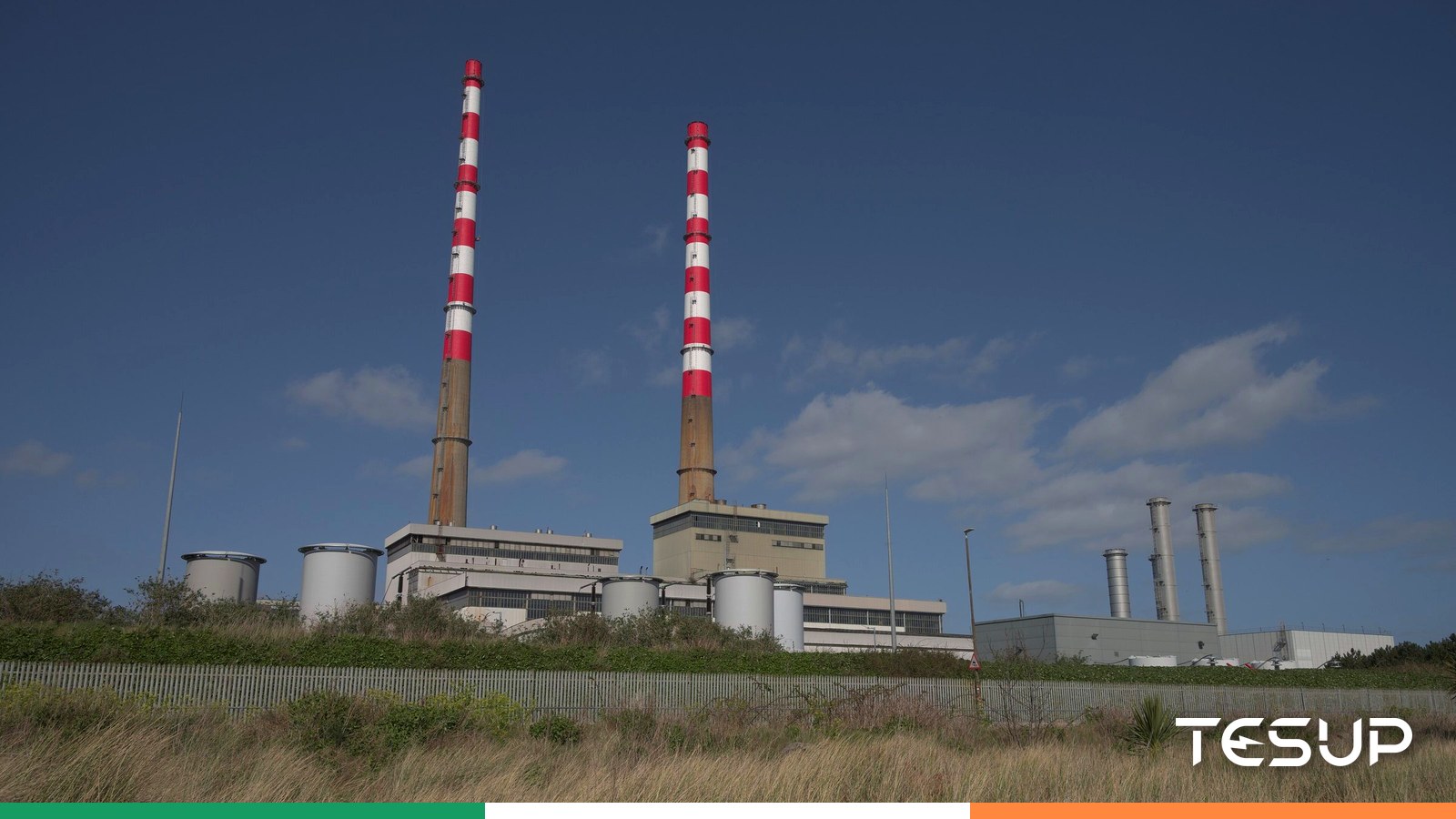 As chaminés vermelhas e brancas de Poolbeg na baía de Dublin sob um céu azul, com uma fita nas cores da bandeira irlandesa
