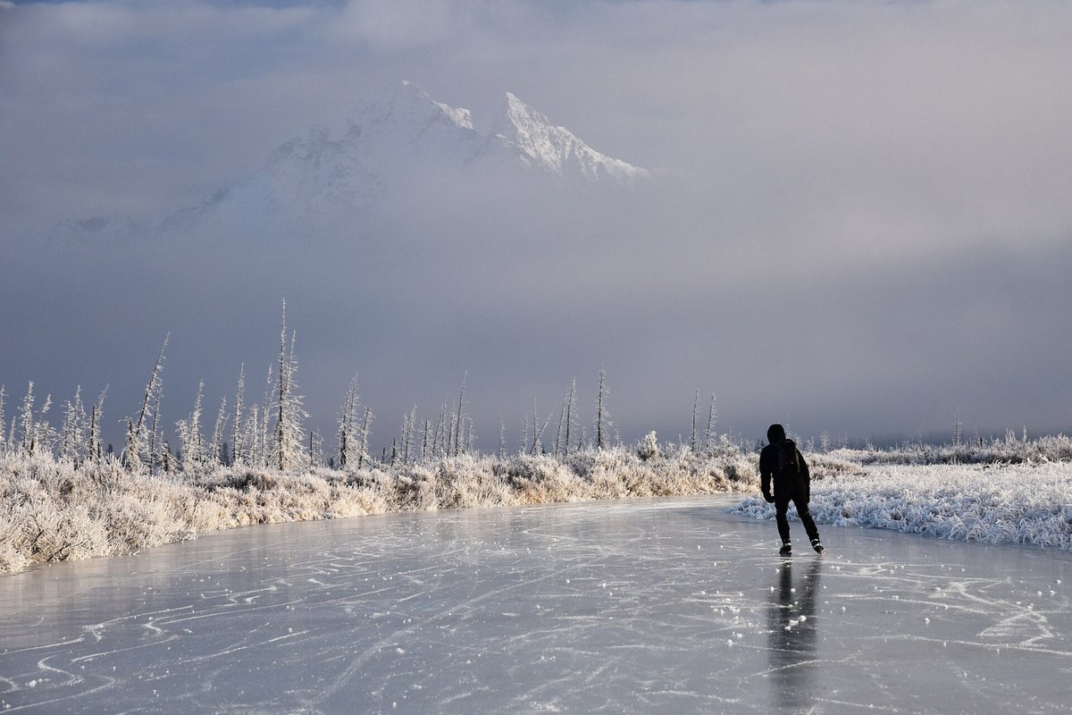A skater on the frozen Rabbit Slough near Wasilla, with frost-covered trees and snowy mountains behind
